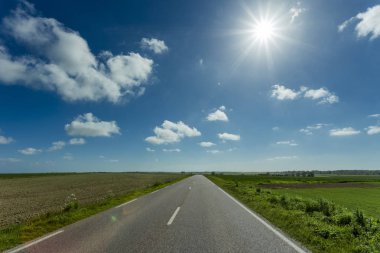 Yeşil ve çiçekli tarım alanları geçerken boş asfalt köy yolunda. Fransa'da bir güneşli bahar gününde kırsal manzara. Çevre dostu tarım, sanayi tarım kavramı