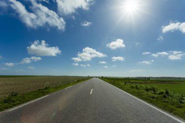 Yeşil ve çiçekli tarım alanları geçerken boş asfalt köy yolunda. Fransa'da bir güneşli bahar gününde kırsal manzara. Çevre dostu tarım, sanayi tarım kavramı