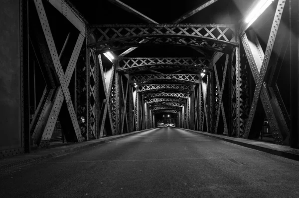 Asphalt road under the steel construction of a bridge in the city. Night urban scene with car light trails in the tunnel. Toned — Stock Photo, Image