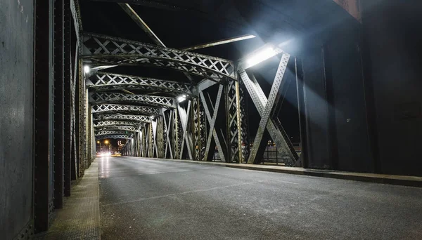 Asphalt road under the steel construction of a bridge in the city. Night urban scene with car light trails in the tunnel. Toned — Stock Photo, Image