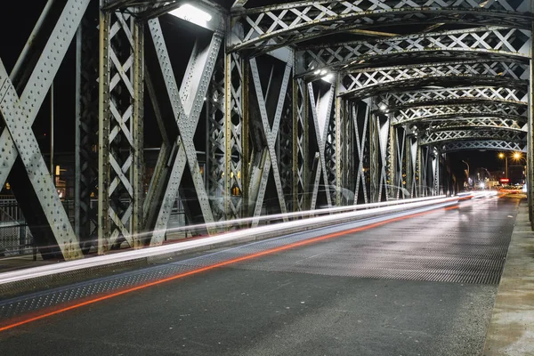 Asfaltweg onder de staalconstructie van een brug in de stad. Stedelijke nachtbeeld met auto licht paden in de tunnel. Toned — Stockfoto