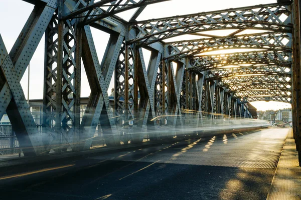 Ασφαλτοστρωμένος δρόμος κάτω από την κατασκευή του χάλυβα από μια γέφυρα της πόλης σε μια ηλιόλουστη ημέρα. Αστικό τοπίο στη σήραγγα γέφυρα. Μακροχρόνια έκθεση. Ήπια — Φωτογραφία Αρχείου