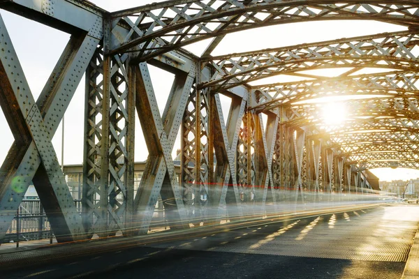 Estrada de asfalto sob a construção de aço de uma ponte da cidade em um dia ensolarado. Cena urbana no túnel da ponte. Longa exposição. Tonificado — Fotografia de Stock