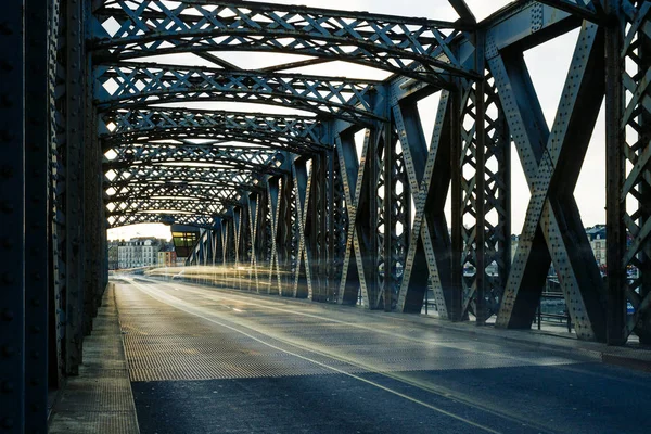 Asphalt road under the steel construction of a city bridge on a sunny day. Urban scene in the bridge tunnel. Long exposure. Toned — Stock Photo, Image