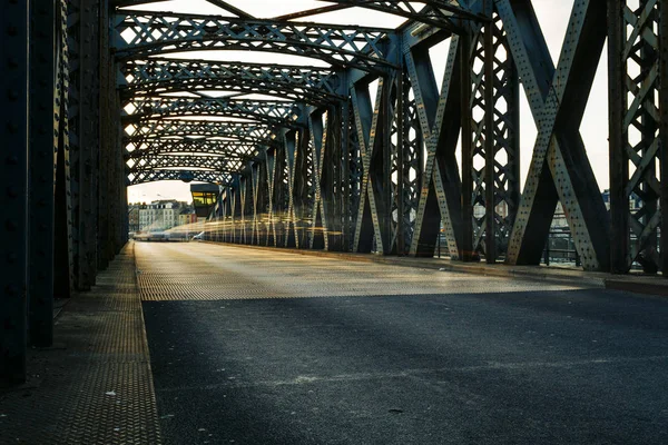 Asphalt road under the steel construction of a city bridge on a sunny day. Urban scene in the bridge tunnel. Long exposure. Toned — Stock Photo, Image