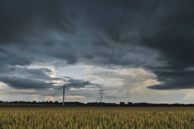 Yüksek gerilim enerji hatları, enerji nakil direkleri ve rüzgar türbinleri bulutlu bir günde tarım alanlarında. Polonyalılar Havai hatları ve siluetleri dusk içinde. Elektrik powere Sanayi ve doğa kavramı.