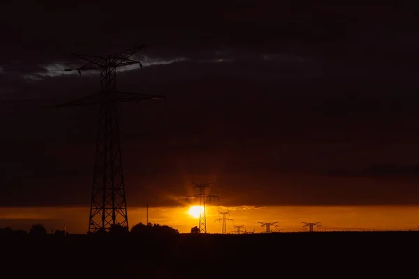 日落时的高压电力线和输电塔。在黄昏中, 波兰人和架空电线的轮廓。发电和配电。电力工业与自然概念 — 图库照片