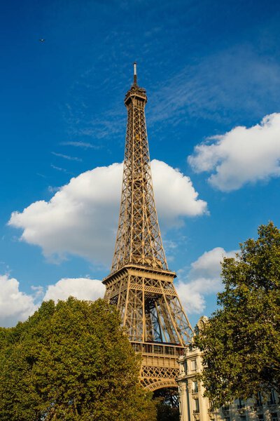 Eiffel tower, Paris symbol and iconic landmark in France, on a sunny day with clouds in the sky. Famous touristic places and romantic travel destinations in Europe. City life and tourism concept.