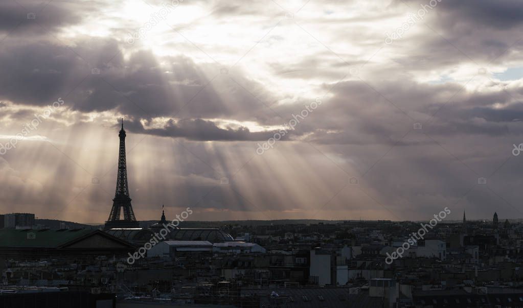 Paris skyline with rooftops and the Eiffel tower on a cloudy day with sun rays. Paris symbol and iconic landmark. Famous touristic places and romantic travel destinations in Europe. Tourism concept