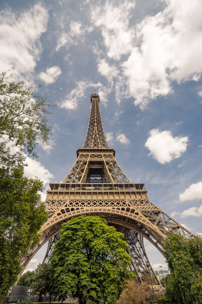Eiffel tower, Paris symbol and iconic landmark in France, on a sunny day with clouds in the sky. Famous touristic places and romantic travel destinations in Europe. Holidays and tourism concept.