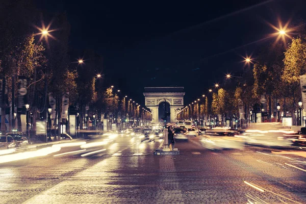 Verlichte Arc de Triomphe en de avenue de Champs-Elysées in Parijs. Bekende toeristische plaatsen en vervoer concept. Nacht stedelijk landschap met straatverlichting van verkeer en stad. Lange blootstelling. Toned — Stockfoto