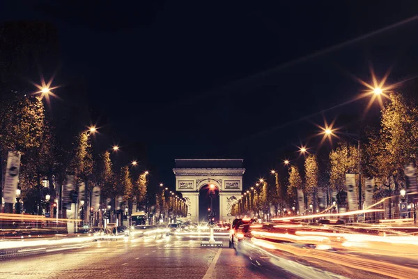 Oświetlony Arc de Triomphe i Alei Pól Elizejskich w Paryżu. Słynnych atrakcji turystycznych i transportu koncepcja. Krajobraz miejski noc z oświetlenia ulicznego ruchu i miasto. Długich ekspozycji. Stonowanych — Zdjęcie stockowe