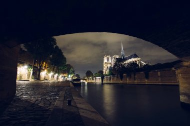 Notre-Dame de Paris gece. Seine Nehri ve şehir ışıkları yansıma iskele üzerinde ünlü antik Katolik Katedrali. Turistik tarihi ve mimari dönüm noktası. Turizm ve seyahat kavramı.