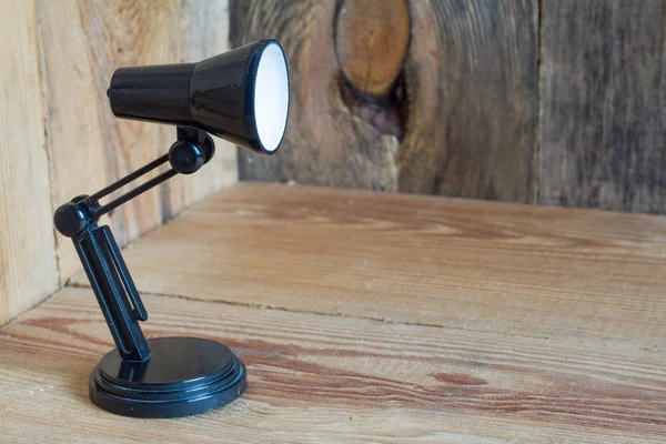 Small table lamp made of black plastic on a wooden background. — Stock Photo, Image