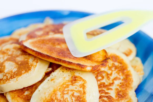 Ruddy panqueques recién hechos se encuentran en un plato azul sobre un fondo blanco . — Foto de Stock