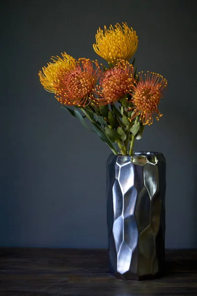 Букет жовтих і оранжевих екзотичних квітів протеїну в металевій вазі на темному фоні, вибірковий фокус — стокове фото
