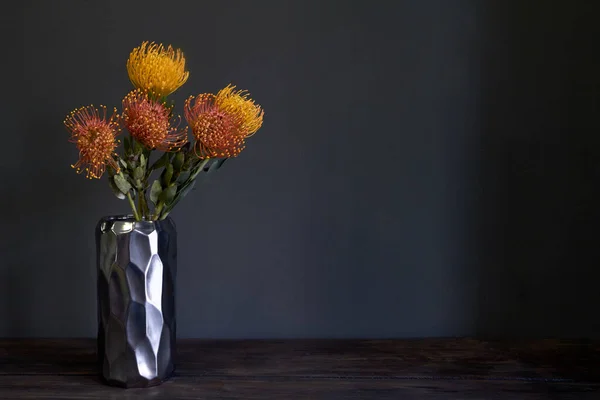 Bouquet of yellow and orange exotic protea flowers in a metal vase on a dark background, selective focus — Stock Photo, Image