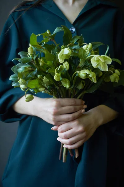 Close-up de uma mulher em um vestido verde segurando um buquê de flores frescas florescendo heléboro, foco seletivo — Fotografia de Stock