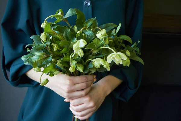 Gros plan d'une femme en robe verte tenant un bouquet de fleurs d'hellébore fraîches, mise au point sélective — Photo