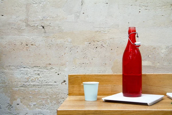 Közelkép egy piros vizes palackról és üvegről az éttermi asztalon, egy fénykő falnak támasztva. — Stock Fotó