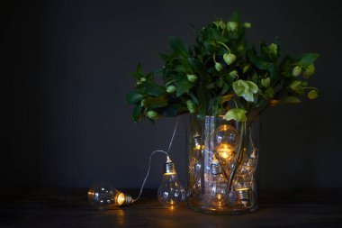 Parlak ampullerle dolu cam vazo ve bir buket hellebore, şenlikli konsept.