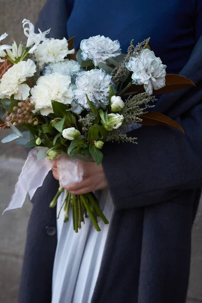 Close-up mãos femininas mantém bouquet tonificado branco em estilo vintage ao ar livre em um fundo de parede cinza, foco seletivo — Fotografia de Stock