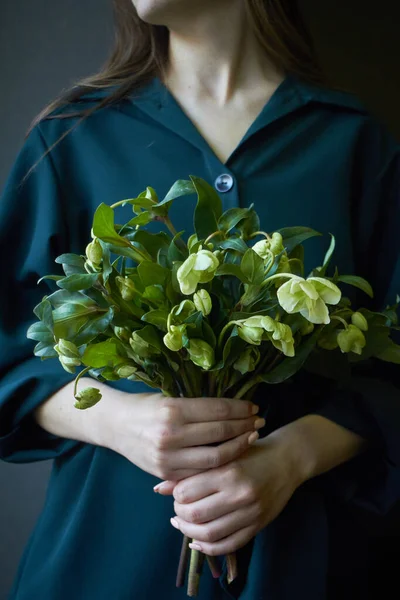 Close-up de uma mulher em um vestido verde segurando um buquê de flores frescas florescendo heléboro, foco seletivo — Fotografia de Stock