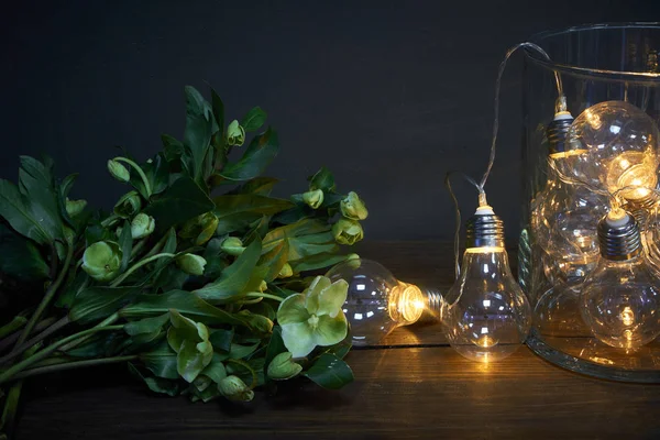 Vaso di vetro pieno di lampadine luminose e un bouquet di elleboro, concetto festivo — Foto Stock