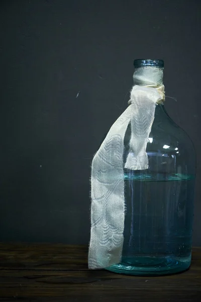 Скляна пляшка або ваза, прикрашена бежевою стрічкою на темному фоні, вибірковий фокус — стокове фото
