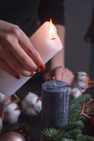 Primer plano de la mano de una mujer vertiendo cera derretida de una vela blanca sobre negro, decoración de la corona de Navidad, enfoque selectivo —  Fotos de Stock
