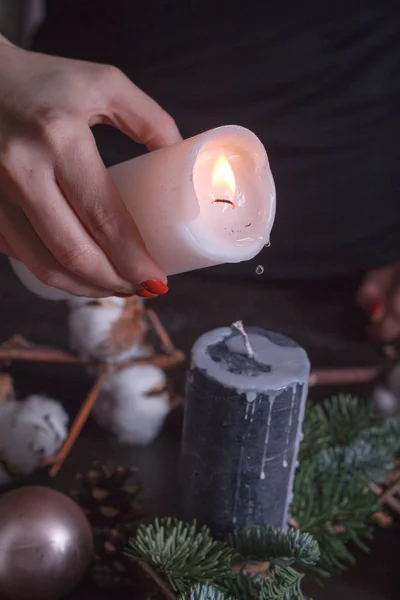 Close-up of a woman's hand pouring melted wax from a white candle onto black, Christmas wreath decoration, selective focus — Stock Photo, Image