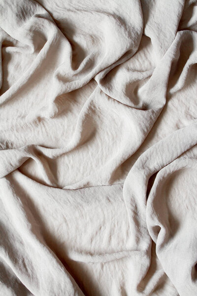 Folds of natural gray beige fabric, top view, background or concept.