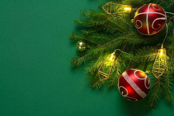 Sfondo o concetto natalizio, rami di abete rosso verde, bolle di Natale rosse e ghirlanda luminosa su sfondo verde — Foto Stock