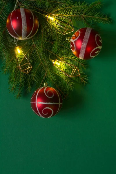 Fundo ou conceito de Natal, ramos de abeto verde, bolhas de Natal vermelhas e guirlanda luminosa sobre um fundo verde — Fotografia de Stock