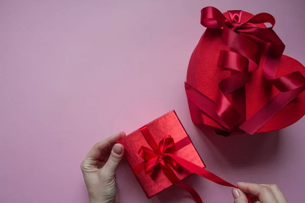 Men's hands wrap red gift box heart shape with red ribbon on a pink background, gift concept