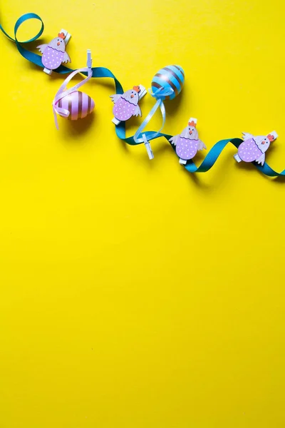 Decoración de Pascua, guirnalda de huevos de colores y figuras de pollo de madera sobre un fondo amarillo brillante — Foto de Stock