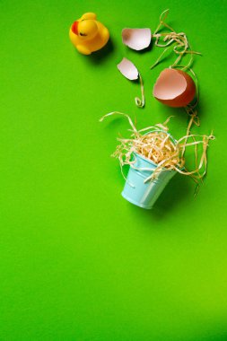Sarı plastik ördek, kırık yumurta kabuğu ve minyatür bir kova, minimalist paskalya arkaplanı ya da konsept
