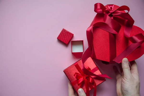 Men's hands wrap red gift box heart shape with red ribbon on a pink background, gift concept