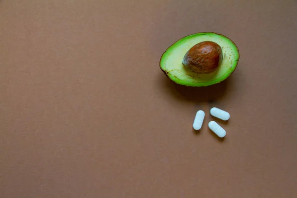Half of raw avocado and pills on brown background, creative food concept