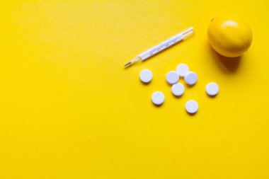 Lemon, sarı arka planda termometre ve beyaz tıbbi haplar, eczane teması, tedavi ve virüsün önlenmesi. Soğuk mevsiminde sağlık kavramı.