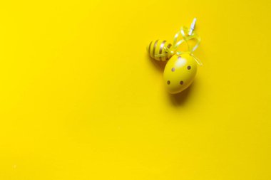 Paskalya süslemesi, iki sarı dekoratif yumurta, parlak sarı arka planda kurdelelerle dikilmiş.