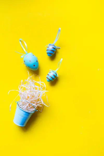 Huevos decorativos de colores y un nido de paja en un cubo en miniatura sobre un fondo amarillo brillante, fondo o concepto minimalista de Pascua — Foto de Stock