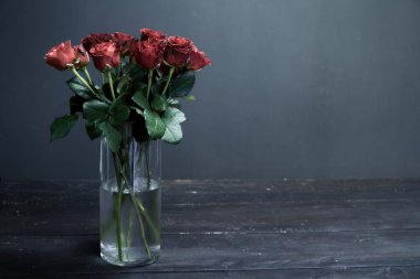 Koyu ahşap bir yüzey üzerinde cam bir vazoda kırmızı-turuncu güller buketi, arka plan veya konsept selamlama
