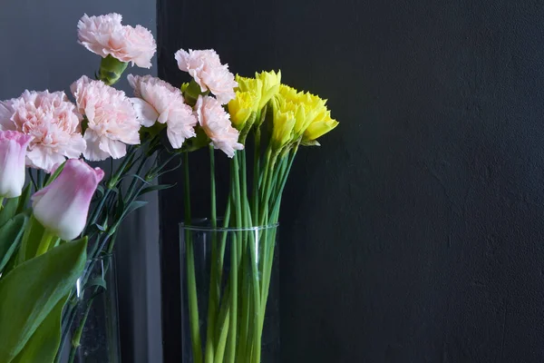 Vasos de vidro com tulipas, cravos e narcisos em um fundo escuro, conceito de parabéns dia da mãe, oitavo de março — Fotografia de Stock