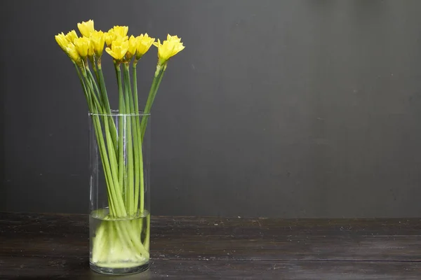 Glass vase with yellow daffodils on a dark wooden table, greeting background or concept — Stock Photo, Image