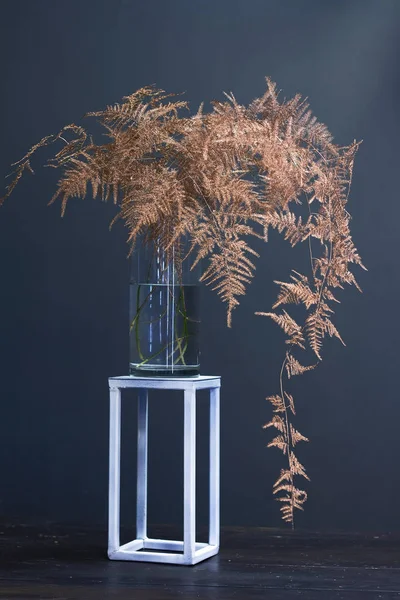 Branch asparagus fern or asparagus setaceus painted in gold in a glass vase on a metal geometric stand, festive background or concept