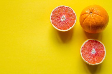 Sarı bir yüzey üzerinde bütün ve dilimlenmiş greyfurt ve portakal, sağlık ve vitamin kavramı.