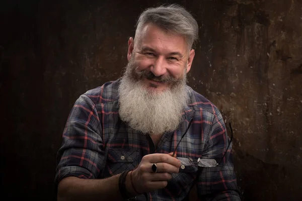 Studio portrait of a gray haired middle-aged bearded man smiles at the camera, selective focus