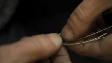 Yakın plan kuyumcu yeni bir ürüne başlıyor, gümüş bir bilezik dokuyor, seçici odaklanıyor.