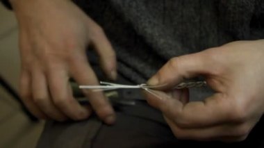 Yakın plan kuyumcu yeni bir ürüne başlıyor, gümüş bir bilezik dokuyor, seçici odaklanıyor.